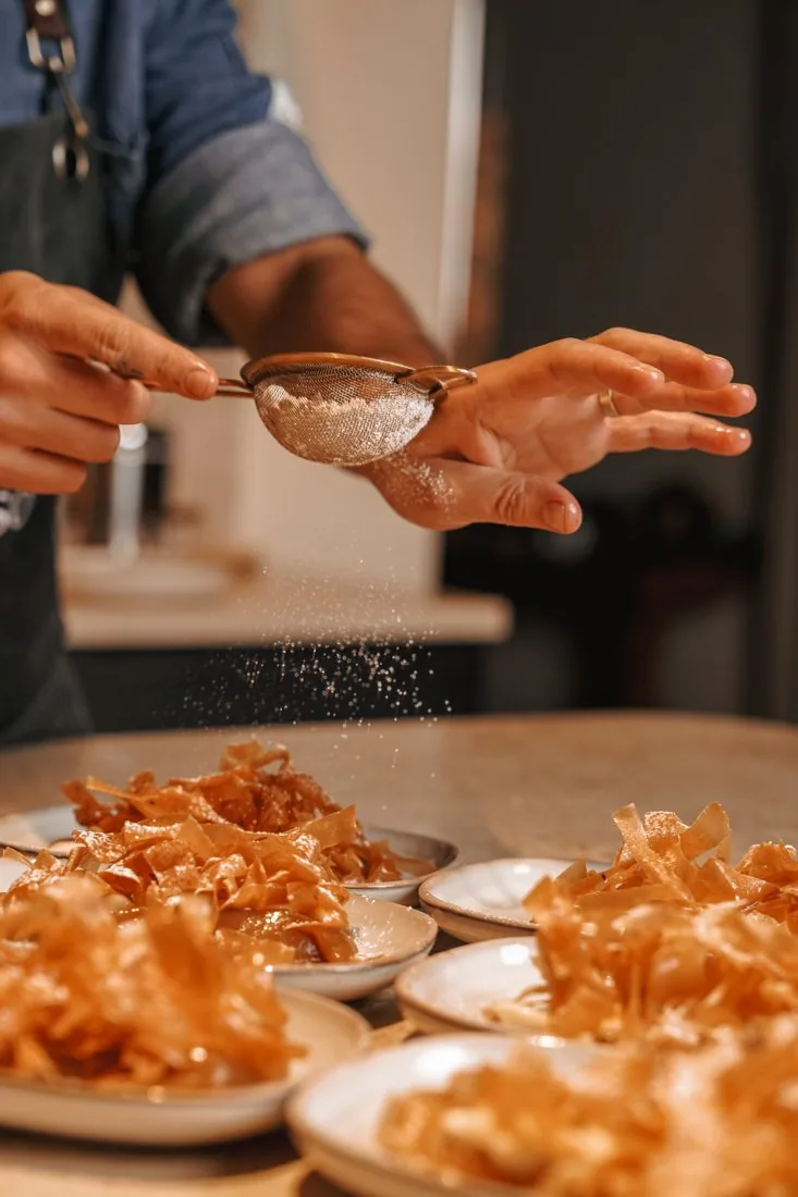 A cook finishing a golden dish in the kitchen at LaMaison