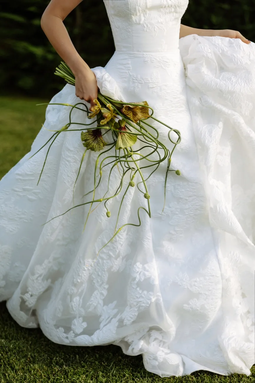 A bride in the garden at LaMaison holding a loose bouquet of seasonal flowers