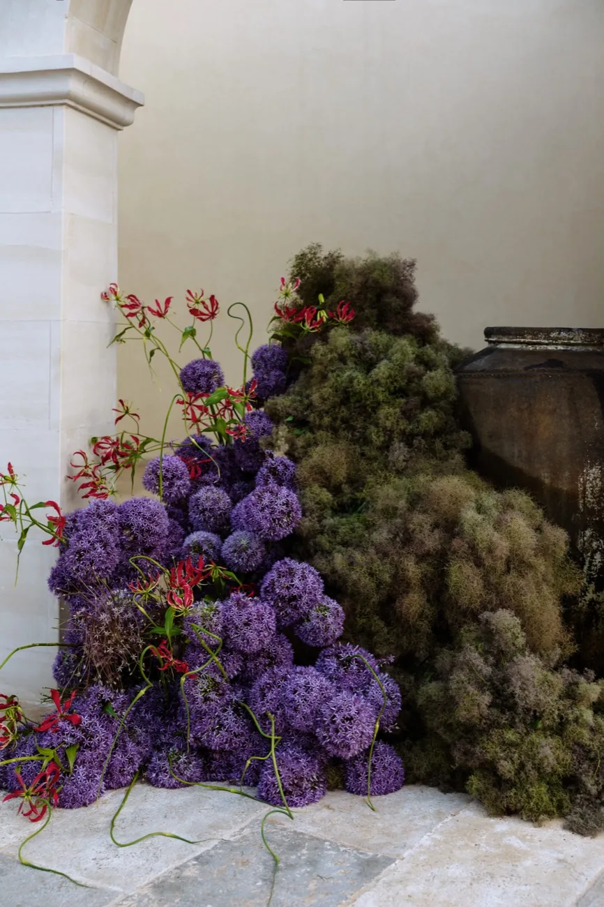 A floral installation of allium and smoke bush against a stone wall at LaMaison